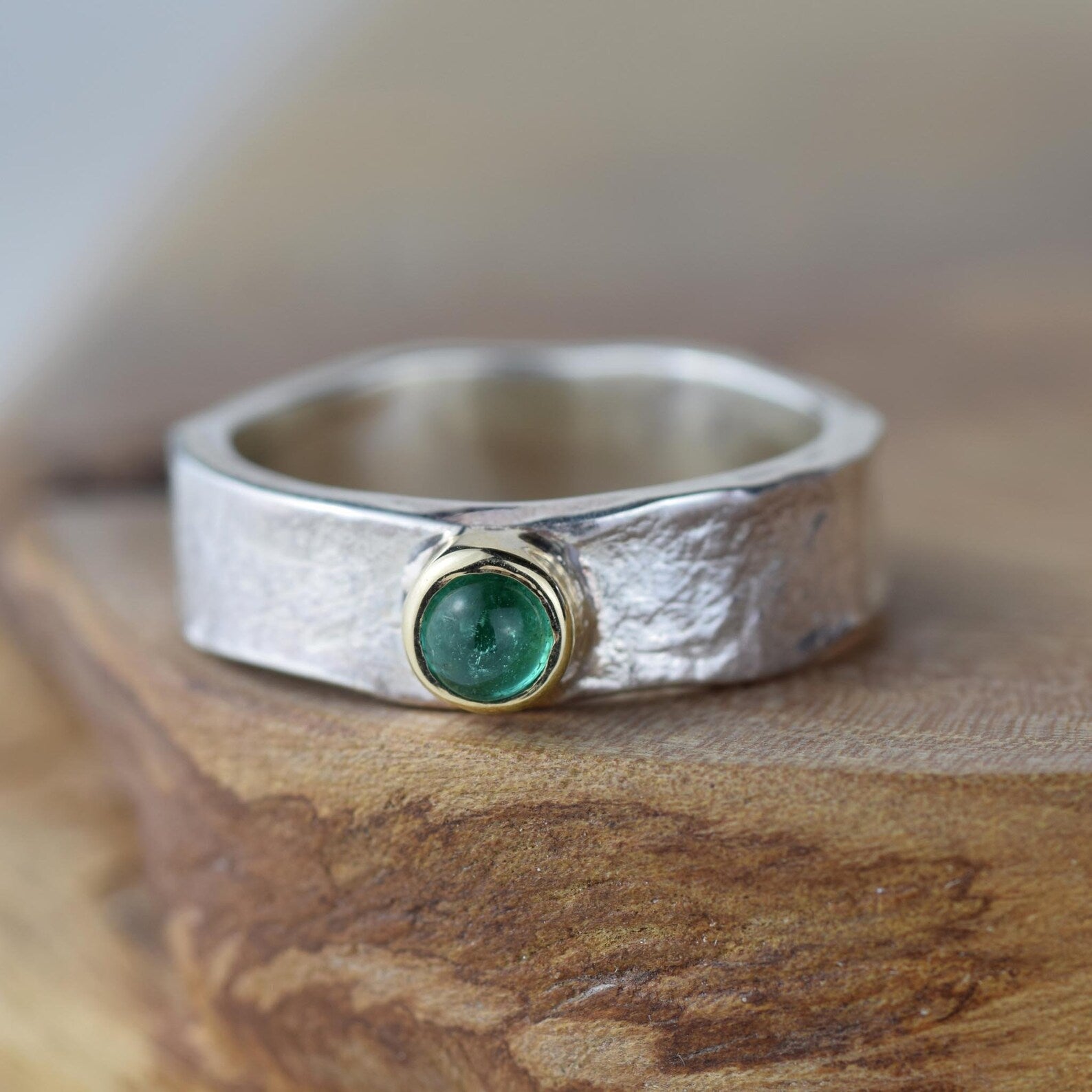 silver ring with a round gold cabochon with a blue tourmaline stone on a wood table